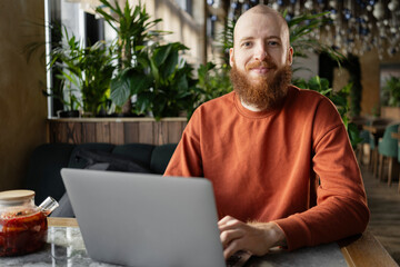 Focused red-haired bearded man millennial sitting at table in cafe. serious businessman freelancer...