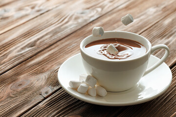 marshmallows falling in cocoa in cup on wooden table