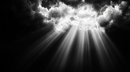 Fototapeta premium Dramatic sunbeams breaking through dark storm clouds in a black and white sky.