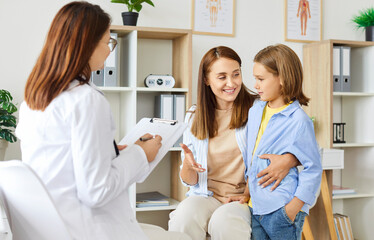 Portrait of a little child girl patient with her mother talking with female cheerful pediatrician...