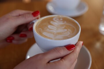 Woman with cup of aromatic coffee at table in cafe, closeup