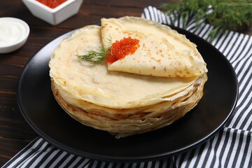 Tasty crepes with red caviar and dill on wooden table, closeup