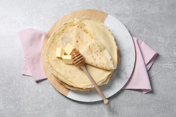 Tasty crepes with butter and honey on grey textured table, top view