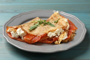 Delicious crepes with salmon, cream cheese and arugula on light blue wooden table, closeup