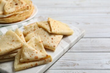 Many tasty crepes on white wooden table, closeup. Space for text