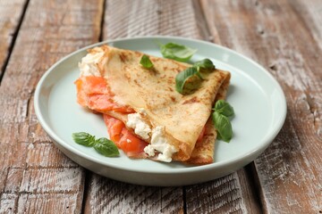 Delicious crepe with salmon, cream cheese and basil on wooden table, closeup