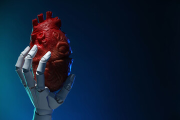 Artificial intelligence. Robot hand holding model of human heart on dark blue background, closeup. Space for text