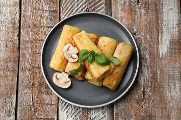 Delicious rolled crepes with mushrooms and basil on wooden table, top view