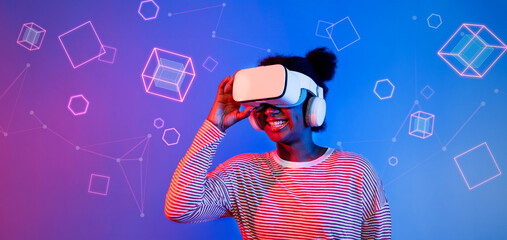 African girl with VR glasses standing at blue and pink background and looking at floating geometric...