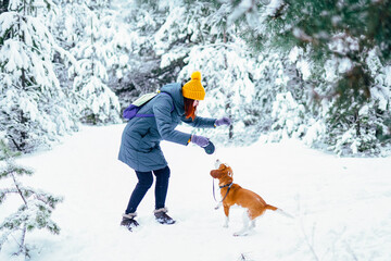 Woman playing with beagle dog in snowy winter forest