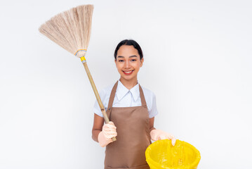 Young female cleaner joyfully holding a broom and a wastebasket, symbolizing cleanliness and positivity. The image features a professional in a brown apron and gloves set against a white background.