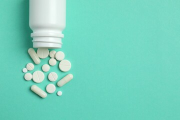 Various pills pouring out of medicine bottle on color background