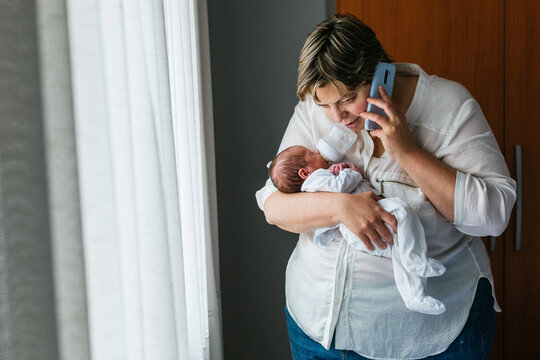 Mother holding newborn son and talking on smartphone