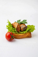 Sardine, mackerel in tomato on a piece of baguette on a lettuce leaf with cherry tomato on a white background. Canned fish.