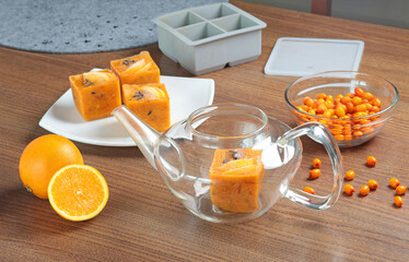 Tea made from frozen briquettes of sea buckthorn, orange and spices in teapot in kitchen. Healthy eating and seasons. Quick beverages to make.