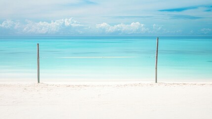 Pristine white sandy beach with two wooden poles framing a tranquil turquoise ocean under a vibrant blue sky, featuring soft clouds and a serene tropical atmosphere.