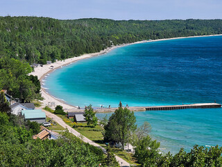 Naklejka premium Looking down on the deep blue and turquoise waters and dock of a bay, surrounded by lush green forests, on a sunny day. 
