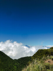 Penetrating the Sky, Mountain Peak View with a Sea of ​​Clouds.The bright blue sky blends with a sea of ​​white clouds that surrounds the lush green valley.