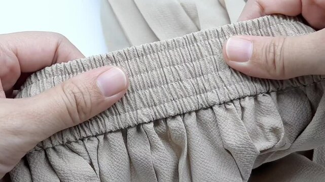 Pulling the elastic waistband of beige pleated pants with both hands