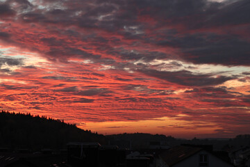 Obraz premium Orange, red sunset over forest and village. Romantic dramatic background for design. Sky and clouds. 