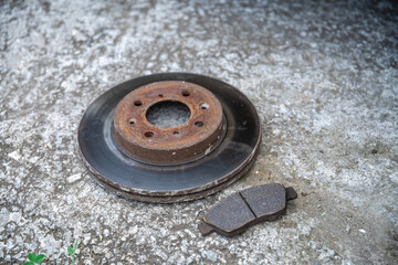 The old brake disc and brake pads are lying on a concrete surface, Repair of the car