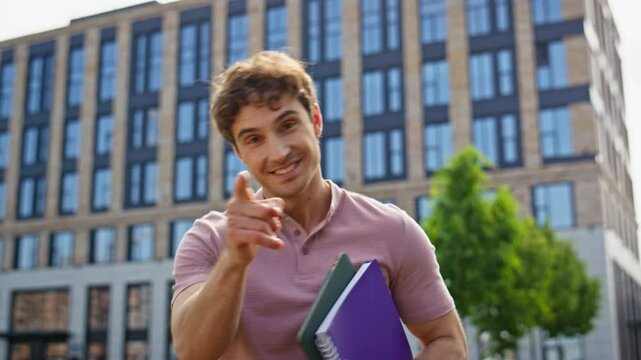 Walking man holding copybooks smiling pointing finger to camera closeup. 