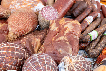 A collection of beautifully arranged cured meats, featuring various types including salami and ham, displayed on a table at a Christmas market. The warm sepia tones enhance the festive atmosphere.