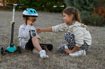 A young boy in a helmet riding a scooter falls and scrapes his knee. A girl approaches him, showing...