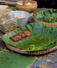 A traditional Indonesian meal, featuring tempeh, rice, and fresh herbs, is beautifully presented on woven baskets and banana leaves, showcasing local culinary traditions.