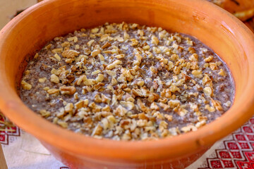 Clay bowl with traditional Ukrainian kutya sprinkled with chopped nuts. The background of the photo is made in folk style with the use of embroidery.