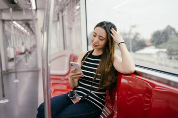Young woman traveling by metro, enjoying the journey while using her smartphone to capture moments...