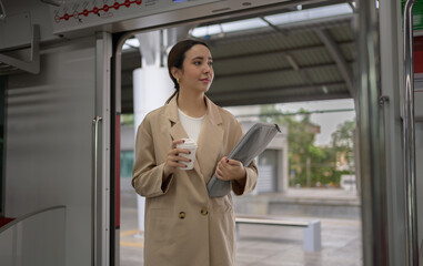 Young businesswoman exiting a train, holding a laptop and takeaway coffee while glancing towards the platform, embodying the hustle of urban commuting in a modern city