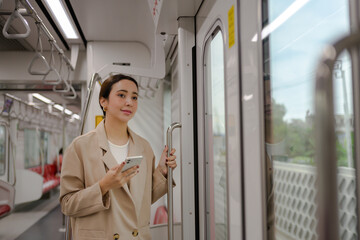 Young businesswoman standing inside a modern train, holding onto the railing while using her...