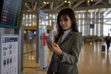 Young asian businesswoman using mobile phone in airport terminal while waiting for her flight...
