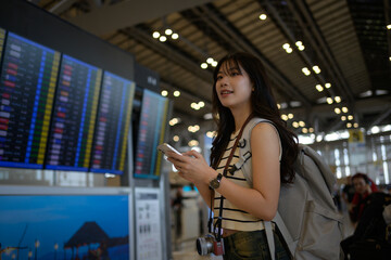Young female tourist with backpack and camera using smartphone checking flight schedule information...