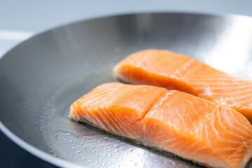 Two raw salmon fillets frying on pan