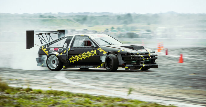 black Toyota AE86 driving sideways at local track driving event. Corolla Sprinter Trueno racecar drifting on concrete surface with smoke coming from rear wheels. Kalynivka, Ukraine - July 26 2014.