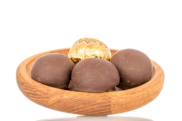 Several chocolate candies wrapped in gift paper with wooden utensils, close-up, isolated on white background.