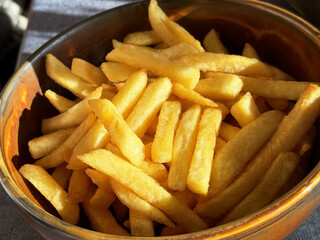 Golden french fries in a bowl under sunlight