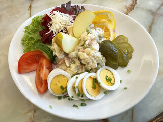 Fresh potato salad with egg, lettuce, tomato, and fruit garnish on a marble table