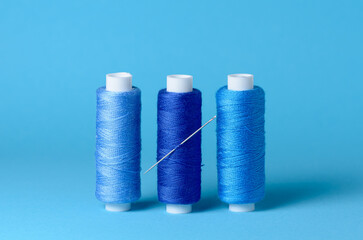 Row of blue thread spools with needle aligned background with copy space for text close-up flat lay top view