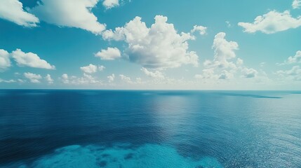 Obraz premium Aerial view captures fluffy clouds contrasting against the serene blue ocean, emphasizing the tranquil beauty of the ocean under a clear sky, with ample copy space.