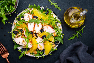 Salad with chicken fillet, juicy orange, sweet raisins, walnut, arugula, spinach and useful seeds, black background, top view