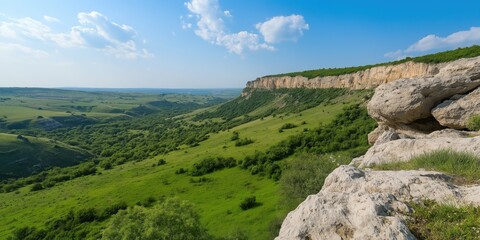 Fototapeta premium A beautiful mountain view with a green grassy hillside. The sky is clear and blue with a few clouds