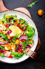 Foodie food salad with baked salmon and tomatoes, cucumber, arugula, radicchio, onion and lettuce with lemon and olive oil dressing.  Brown background, top view
