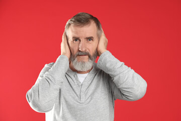Senior man covering his ears on red background