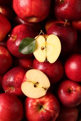 Fresh ripe red apples and green leaves as background, top view
