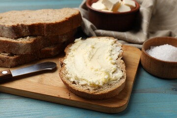 Fresh bread with butter, salt and knife on blue wooden table, closeup