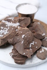 Pieces of tasty chocolate with salt on white table, closeup