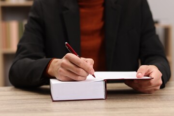 Writer signing autograph in book at wooden table indoors, closeup